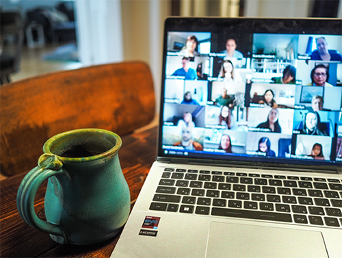 PC laptop with a group call onscreen and a mug of coffee on a desk in a livingroom